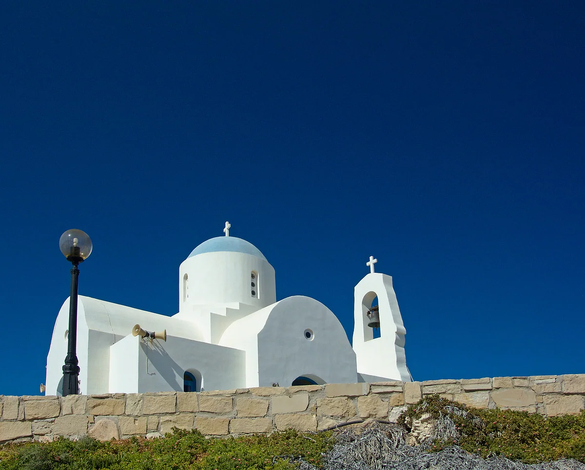 The white chapel of Agios Nikolaos at Pernera, with its blue dome and bell gable, above a stone wall against a deep blue sky