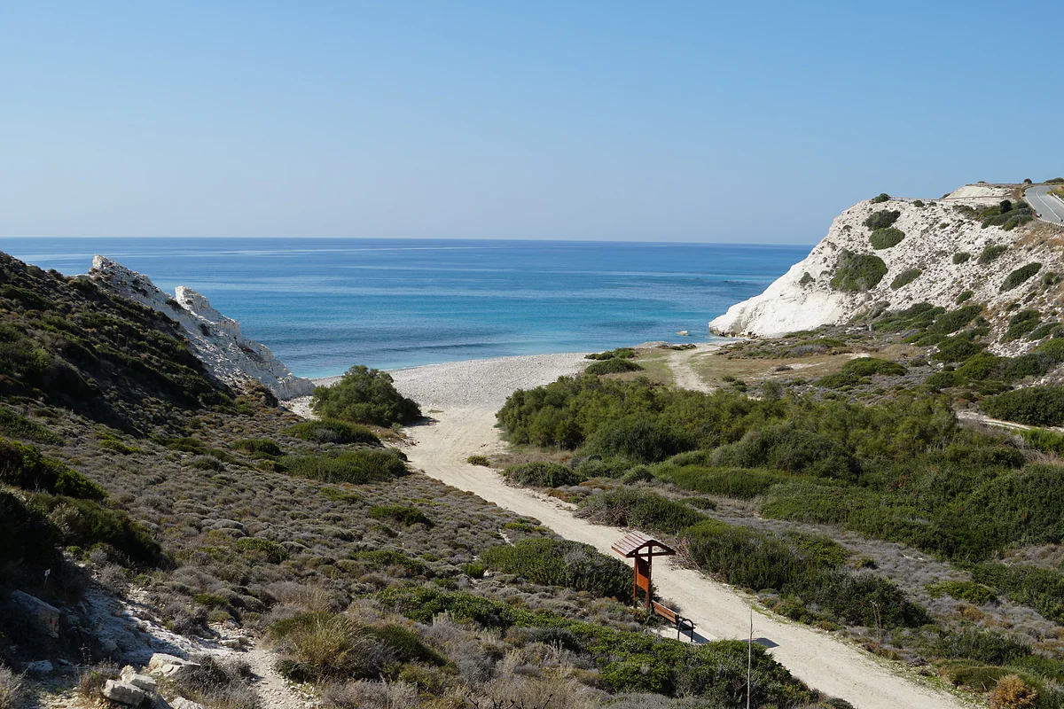 A dirt track runs down through scrub to a beach at Pissouri, with white cliffs on one side and a blue sea
