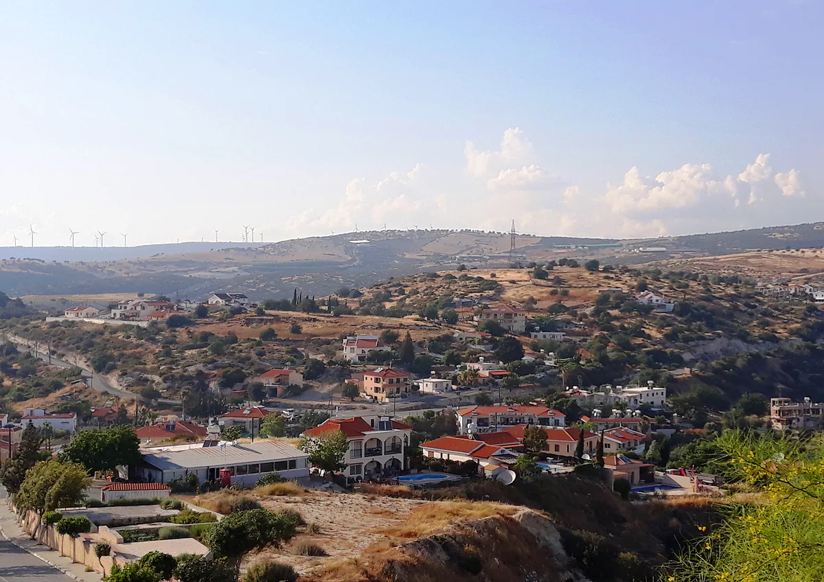 Pissouri village on its green hillside, with white houses and red roofs and wind turbines on the skyline