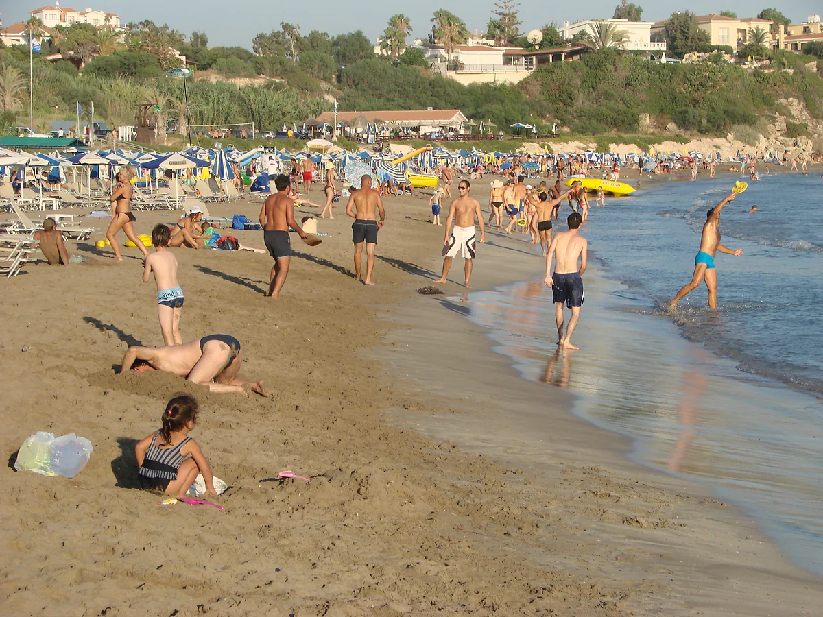 The sandy beach at Coral Bay in Pegeia, with swimmers, sunshades and houses on the slope behind, north of Paphos, Cyprus