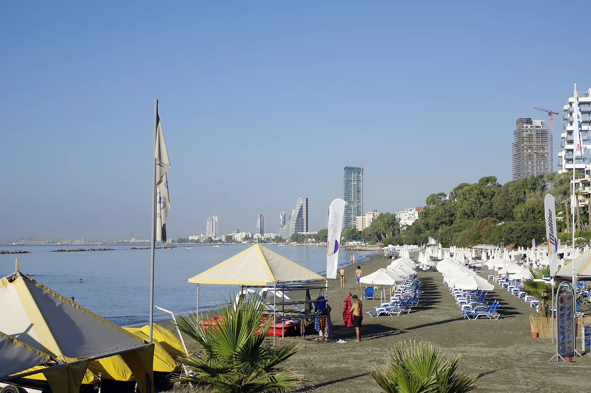A Limassol beach in the morning, with sunbeds, parasols and the city's tower blocks lining the coast