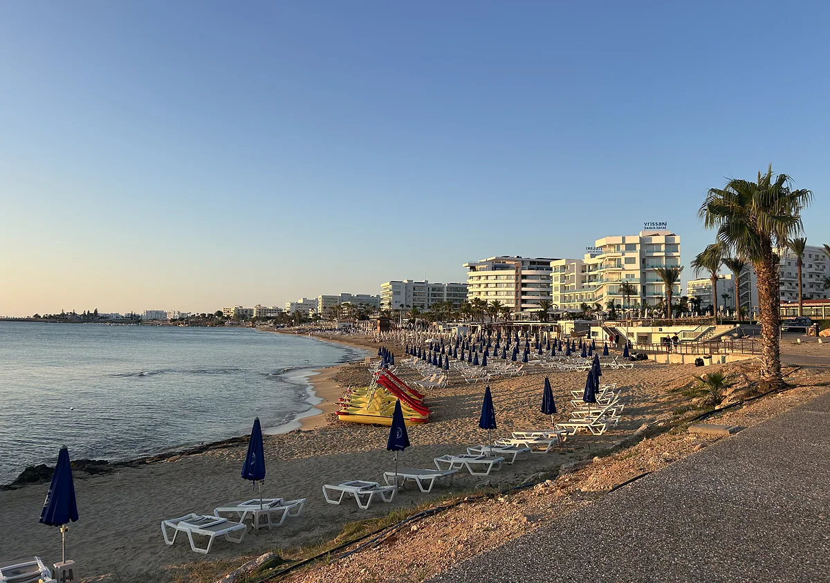 Protaras beach at dusk, with parasols, sunbeds, palm trees and the seafront hotels behind