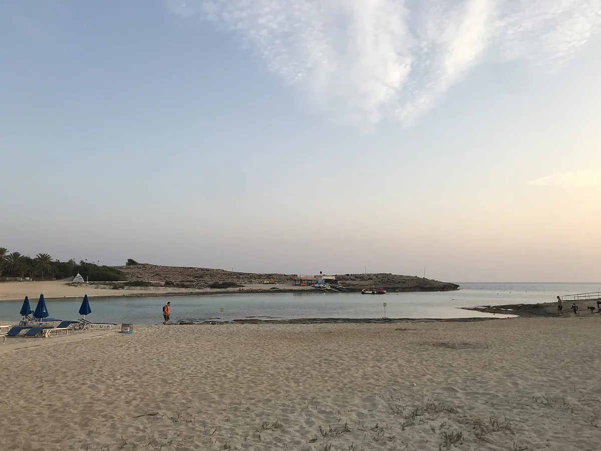Vathia Gonia beach in Ayia Napa, with pale sand, a few parasols and a spit of rock running into the sea