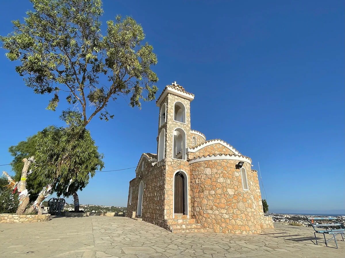 The bell tower and golden stone front of the Profitis Ilias chapel, high on its hill above Protaras, under a clear blue sky