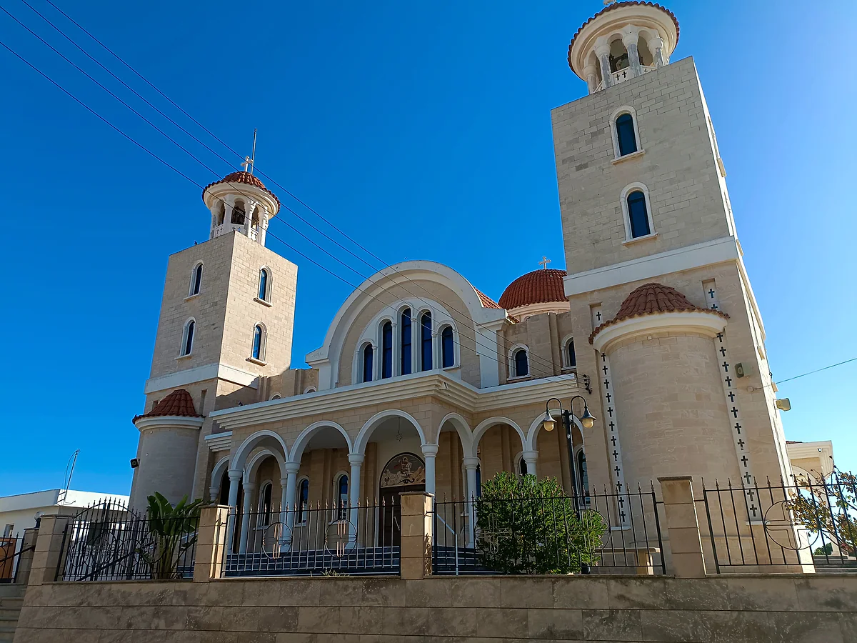 The church of St George in Pyla, in pale stone with an arcaded porch, red dome and two bell towers under a blue sky