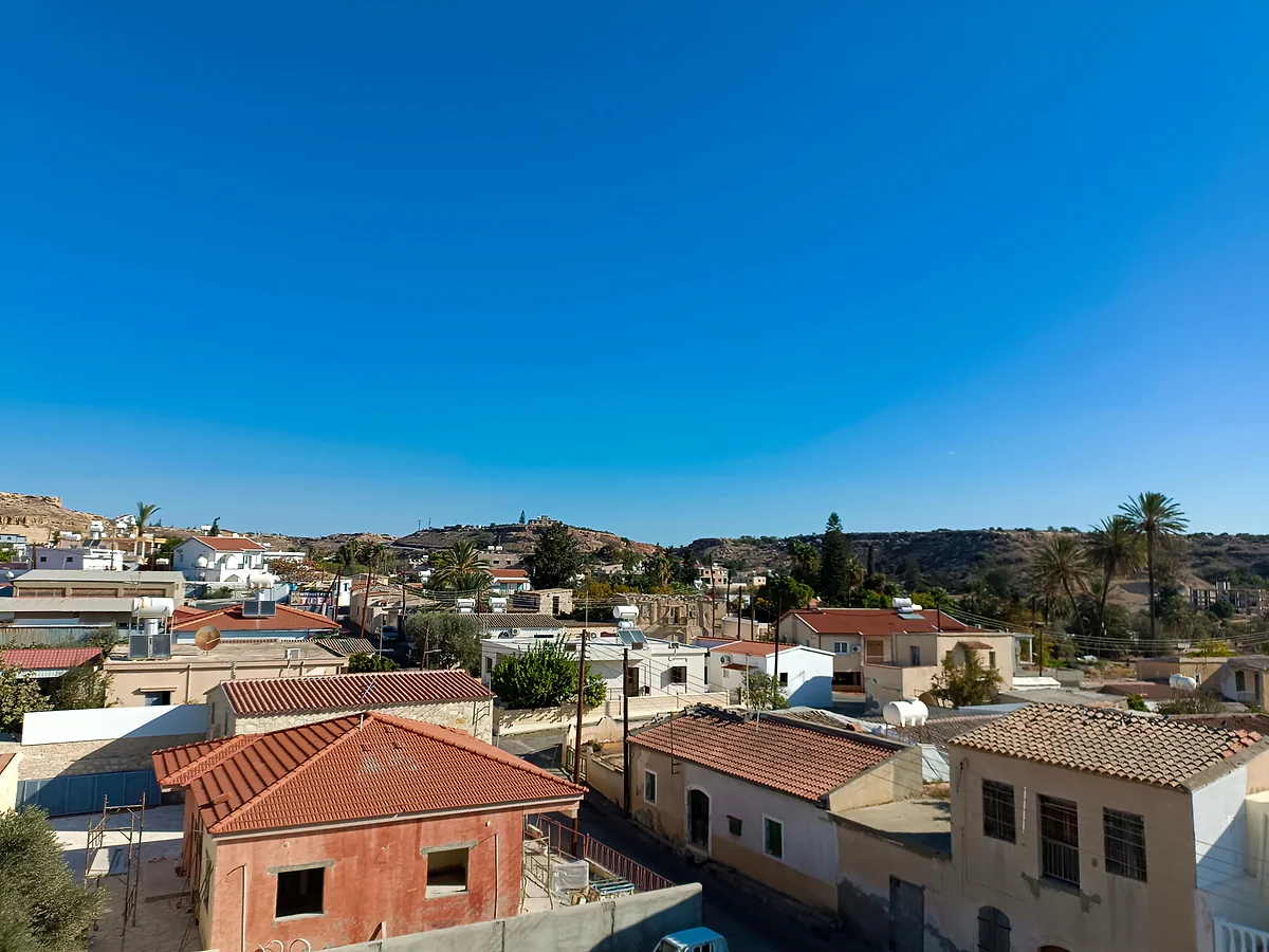 Pyla from above, with low houses with flat and red roofs, palm trees and gentle hills on the horizon