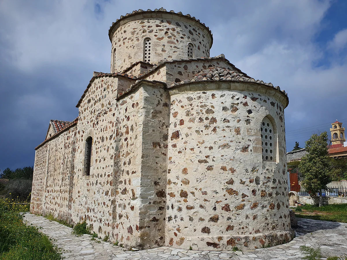 A stone church with a dome and rounded apse in Pyrga, under a cloudy sky, with the village behind it