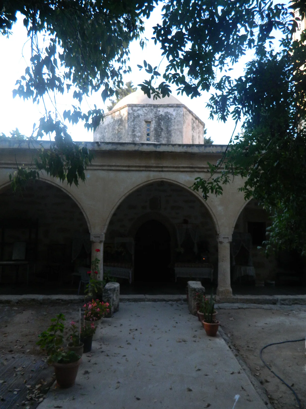 The stone arcades of the old church of the Transfiguration in Sotira, with its dome rising behind the trees