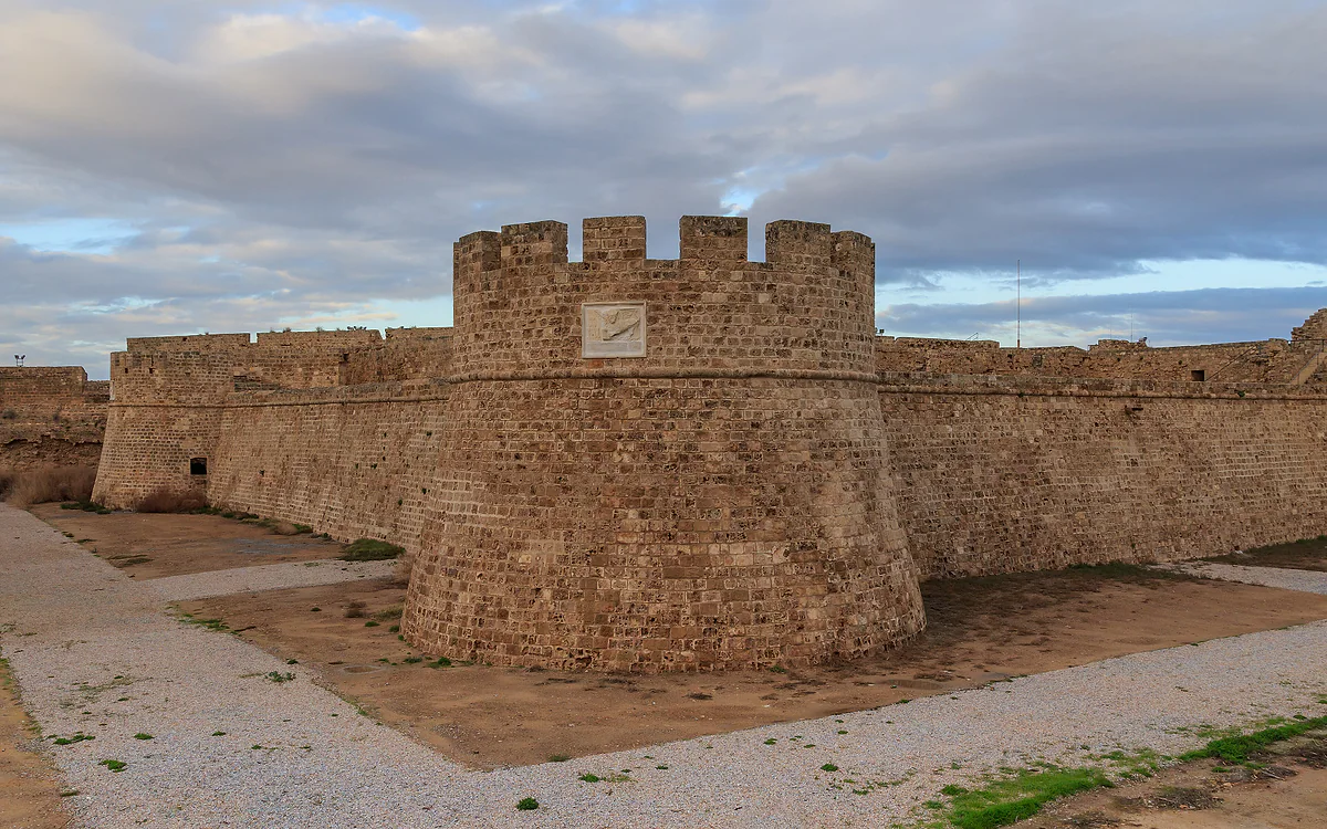 The round tower of Othello's citadel in Famagusta, with battlements, the Lion of Venice relief and the dry moat below