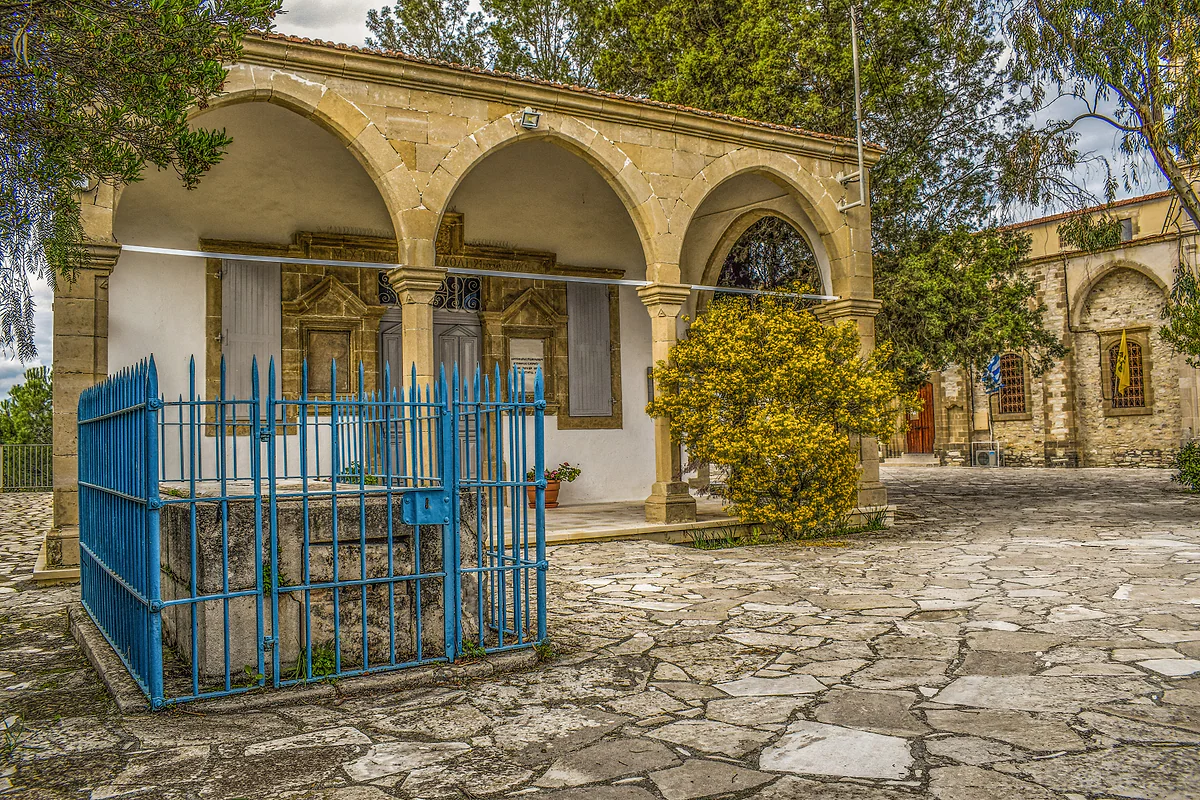 An arcade of yellow stone arches in Vavla, with a blue railing in front and a floor of stone flags