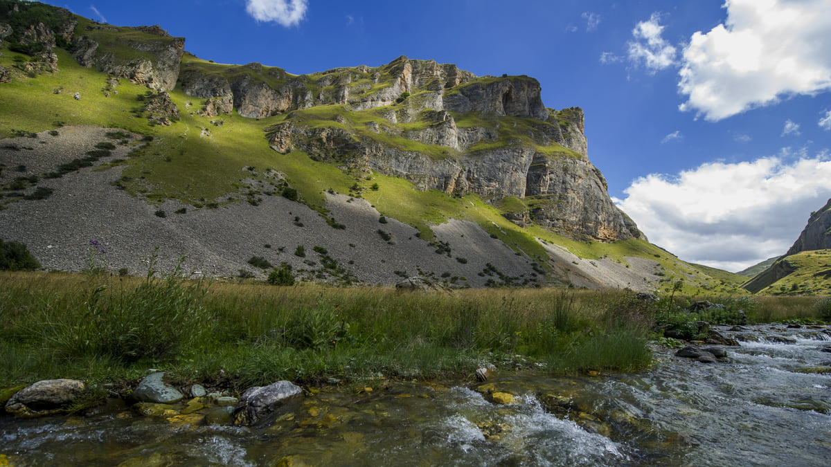 A mountain stream near Brod in Dragash, with green meadows and tall rock faces under a blue summer sky