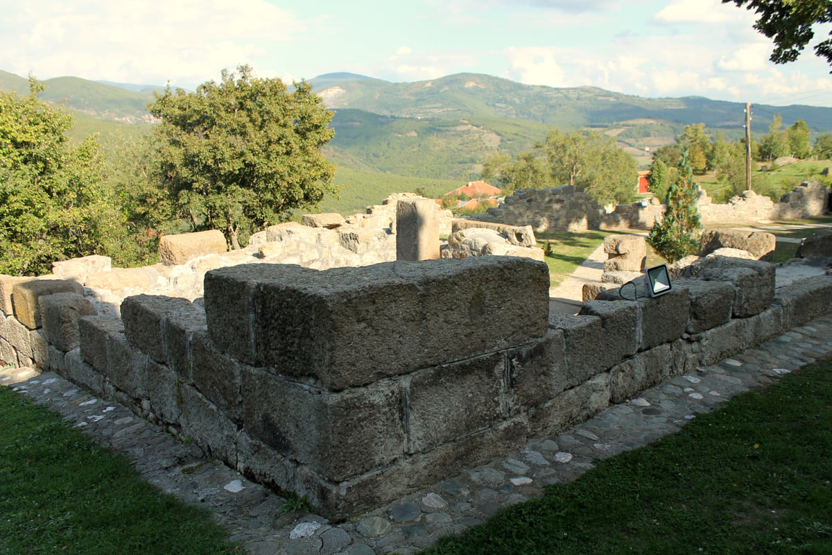 Dressed stone walls of the Isa Boletini kulla complex in Boletin, with a grassy courtyard and wooded hills in the distance