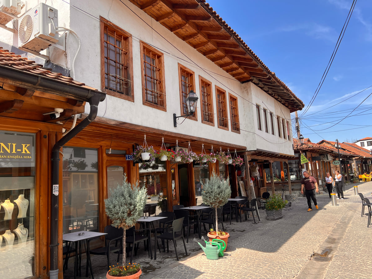 A street in the Grand Bazaar of Gjakova lined with two-storey timber houses, café terraces and potted olive trees