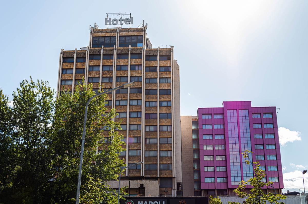 The 1970s tower of the Grand Hotel Pristina, with its concrete facade and a pink building beside it
