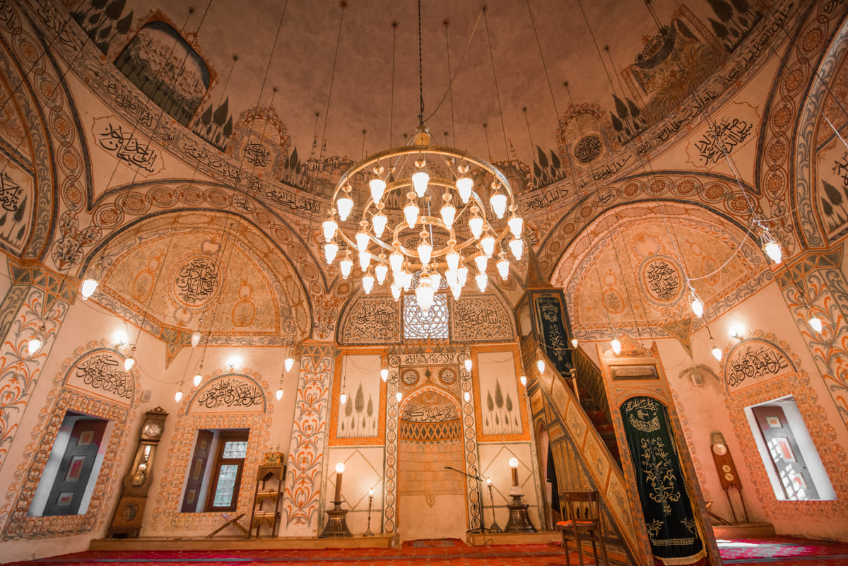 The interior of the Hadum Mosque in Gjakova, with walls painted in ochre tones and a large hanging chandelier