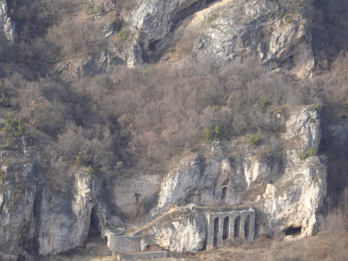 The hermitage of St Peter at Korisha, set into a rock face with stone arches and walls among dry scrub