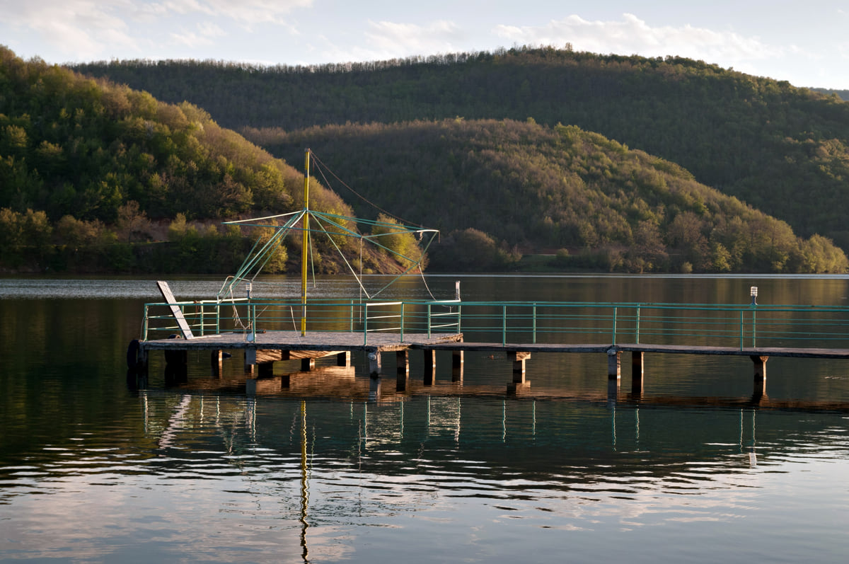 A wooden jetty on Lake Batlava, with calm water and forested hills rising behind it on a bright day