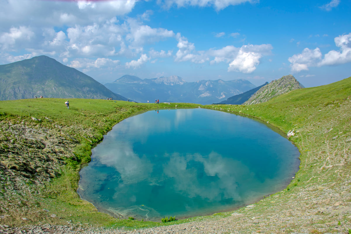 A round blue mountain lake set in the high pastures above Junik, with peaks in the background