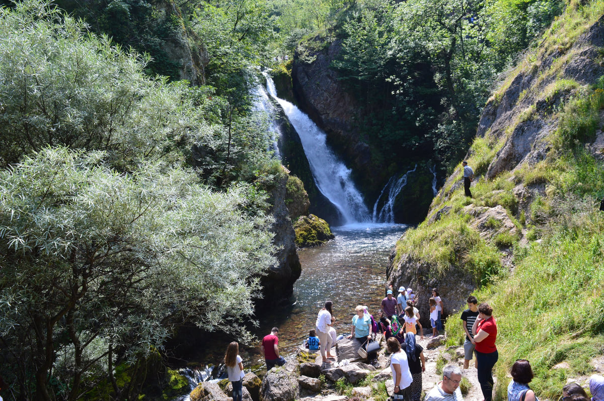 Water from the source of the White Drin at Radavc falling down the rock among trees, with visitors below