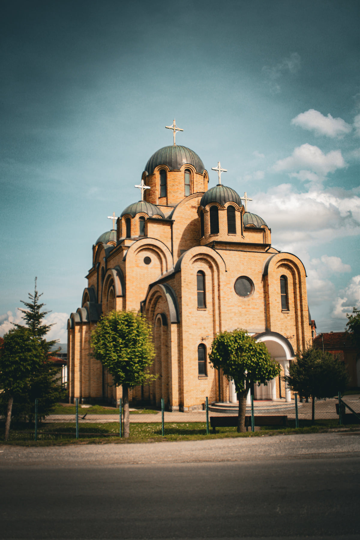 Holy Trinity Orthodox church in Partesh, in yellow brick with green domes, behind a low fence and young trees