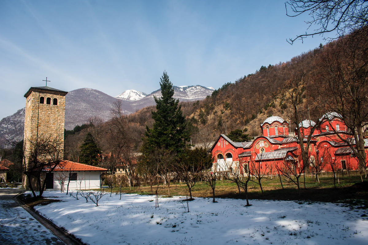 The red churches of the Patriarchate of Peć beside a stone tower, with snow-covered mountains behind in winter