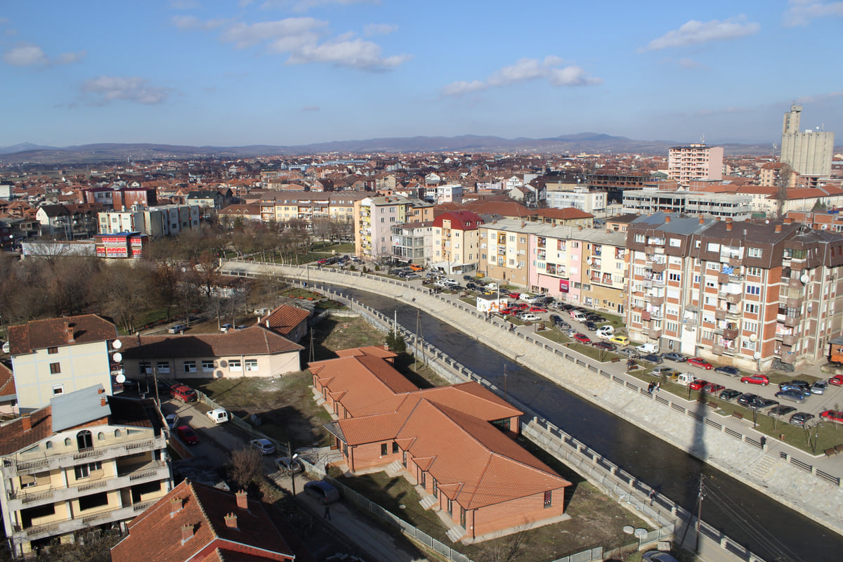 Podujeva seen from above, with the channelled river running between blocks of flats, red roofs and hills behind