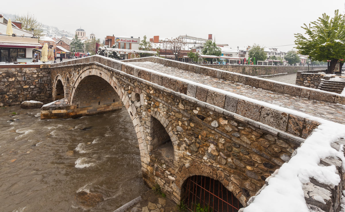The single pointed arch of Prizren's Ottoman stone bridge over the Bistrica river, framed by trees