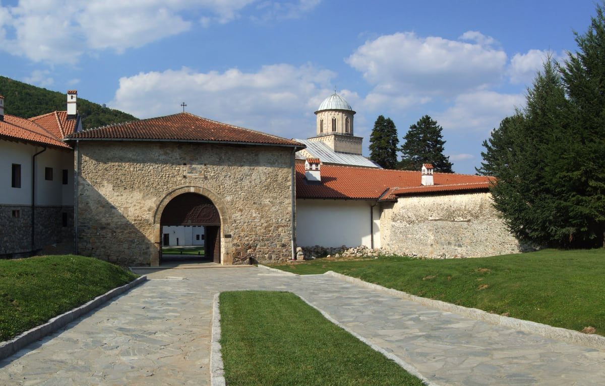 The main gate of Visoki Dečani Monastery, a stone archway with a tiled roof and the bell tower behind