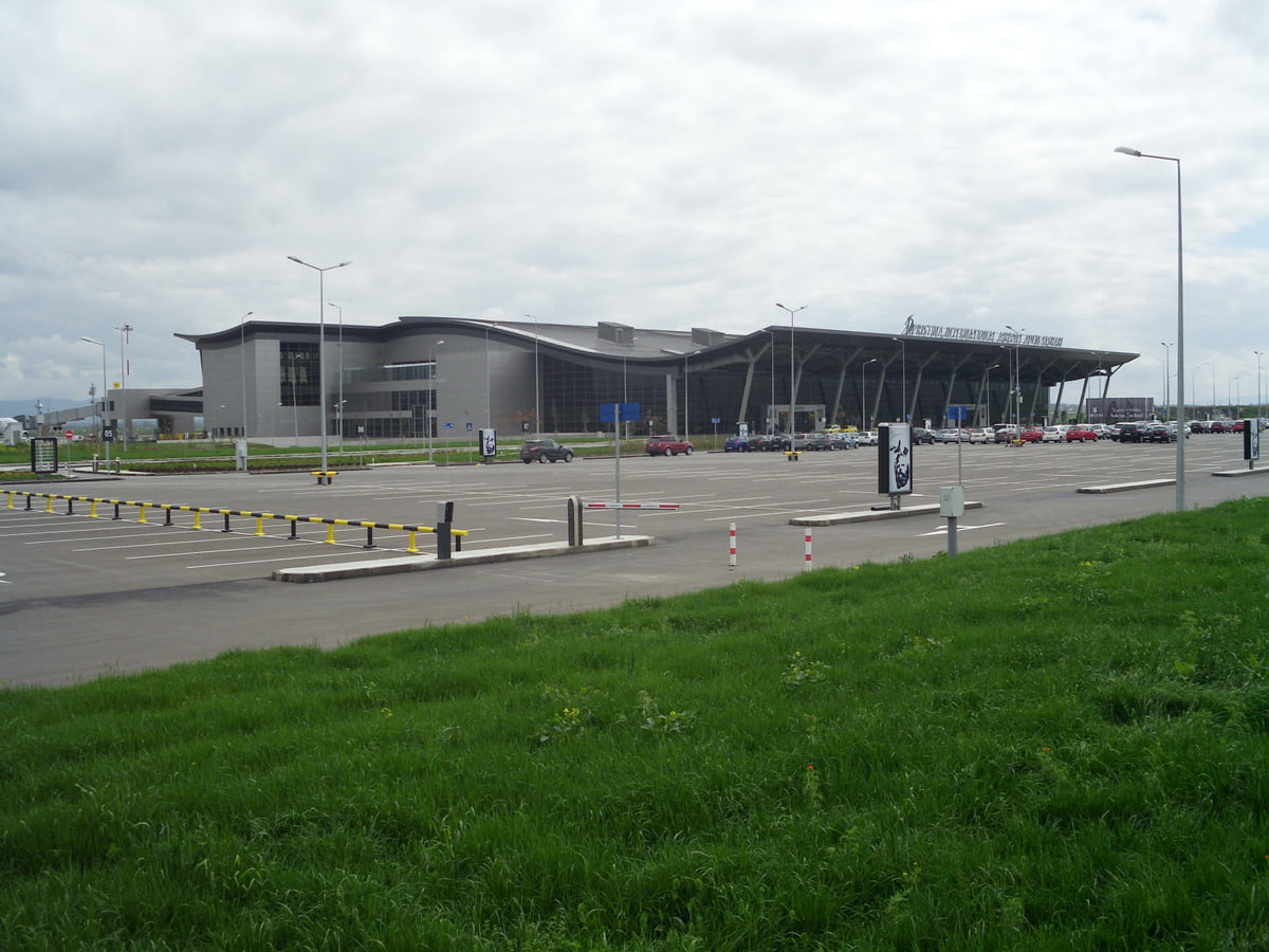 The terminal of Pristina International Airport, a low glass-and-metal building beyond a strip of grass