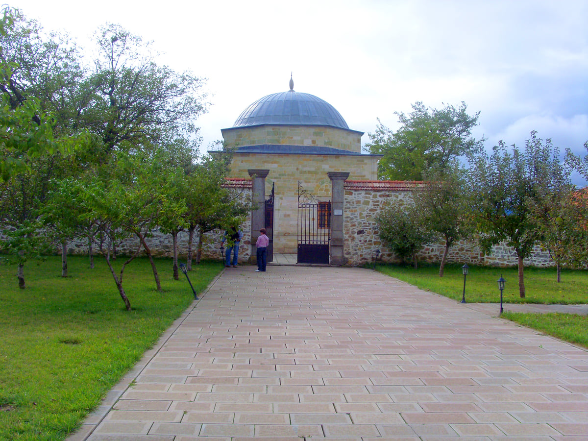 The tomb of Sultan Murad I at Mazgit in Obiliq, its lead dome behind a stone wall at the end of a path lined with fruit trees