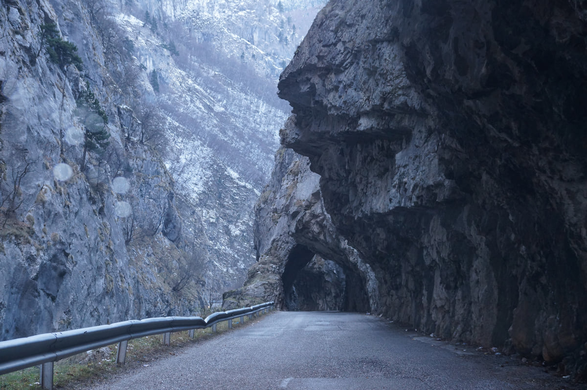 The Rugova Canyon road running into a tunnel cut through the rock, between sheer limestone walls