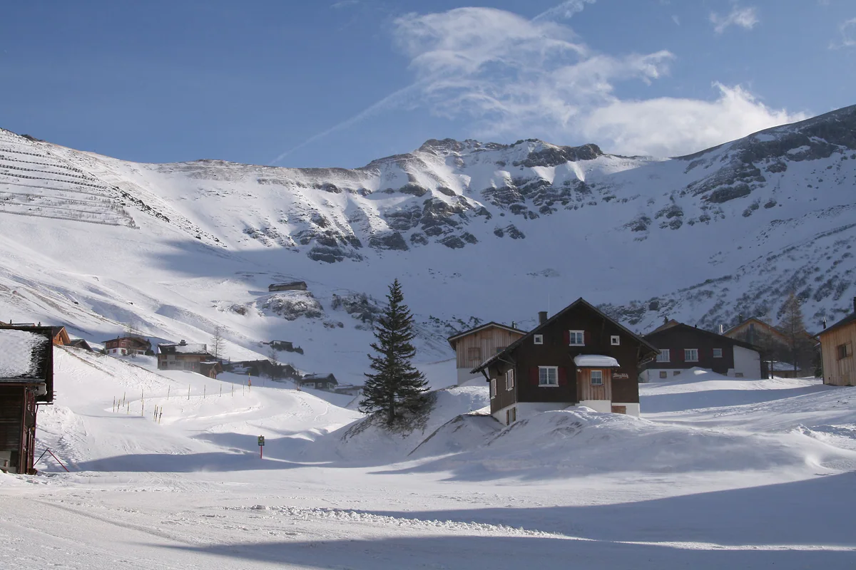 Malbun nevado, con chalés de madera, un abeto y las pistas de esquí bajo las cumbres blancas.