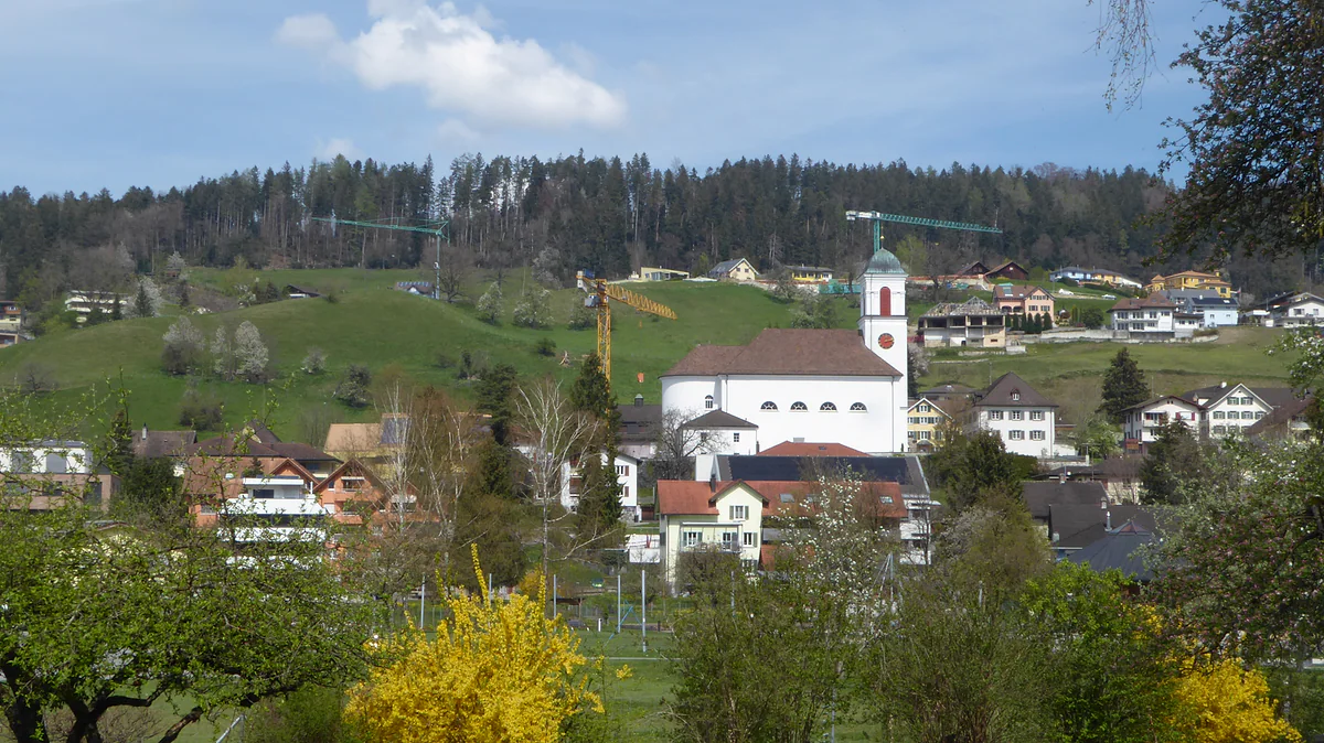 Mauren visto desde el sur, con la iglesia blanca en la colina, las casas entre los árboles y el bosque detrás.