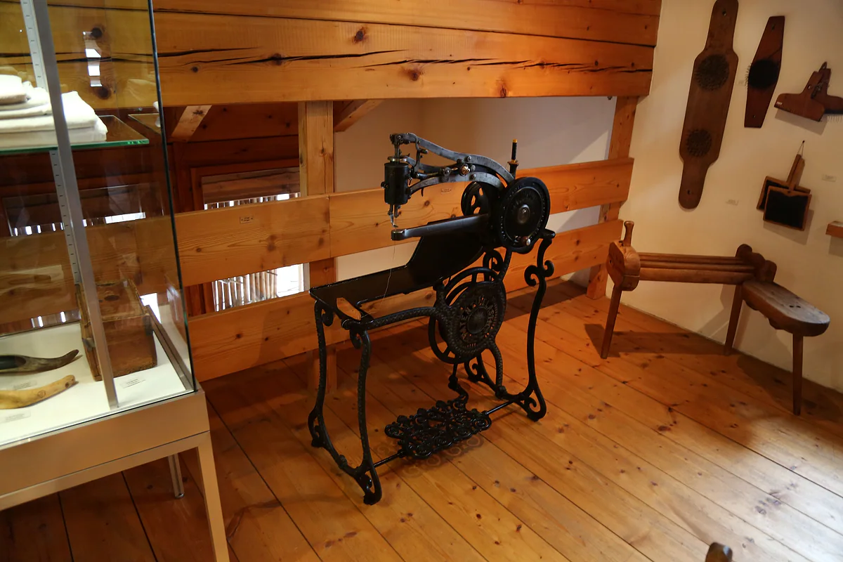 Una sala del Walsermuseum de Triesenberg, con suelo y paredes de madera, una máquina de coser antigua y herramientas colgadas.