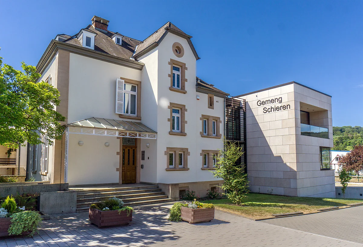 Schieren town hall, a pale villa with bay windows and a modern stone extension, with flowers at the entrance