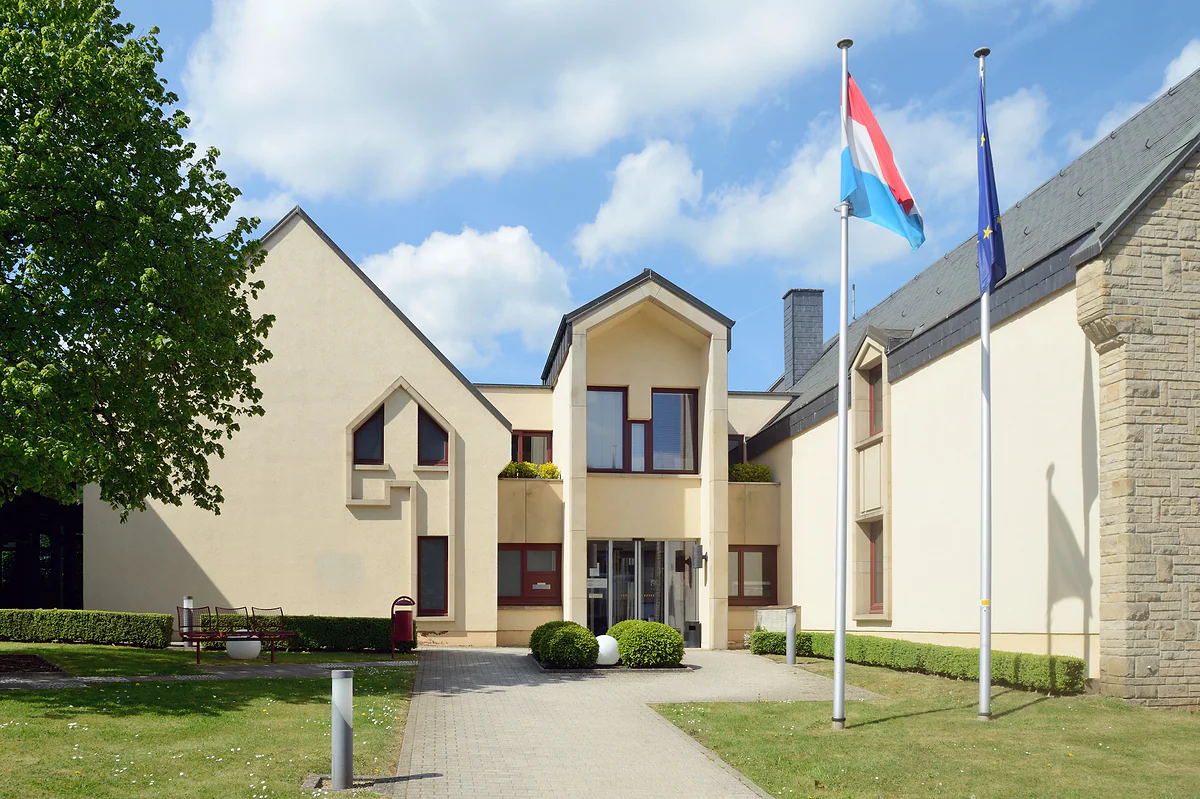 Steinsel town hall, with gabled façades, a lawn in front and the flags of Luxembourg and the EU