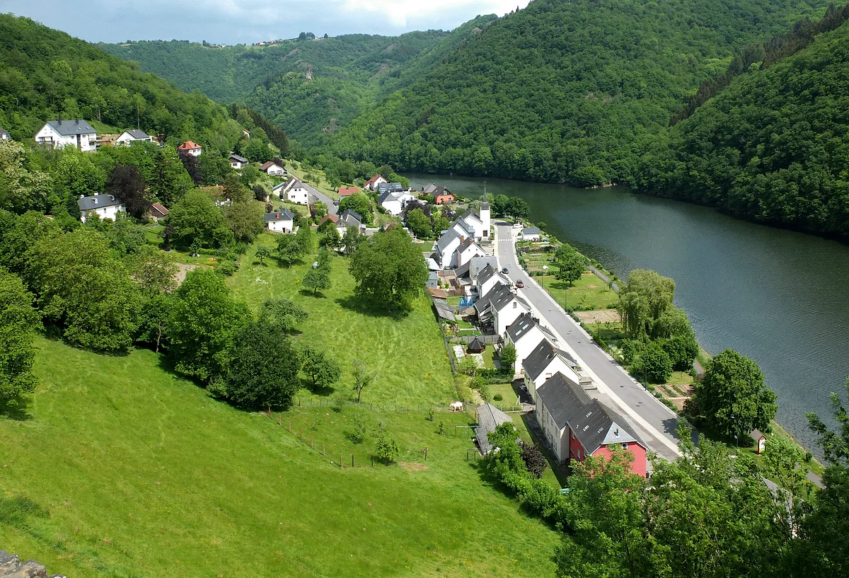 The village of Bivels on a bend of the River Our, with houses lined up by the water and lush forested slopes
