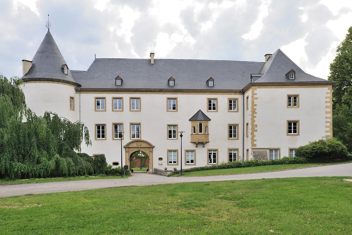 Sanem Castle, with a pale façade, round towers with conical roofs and a broad lawn in front