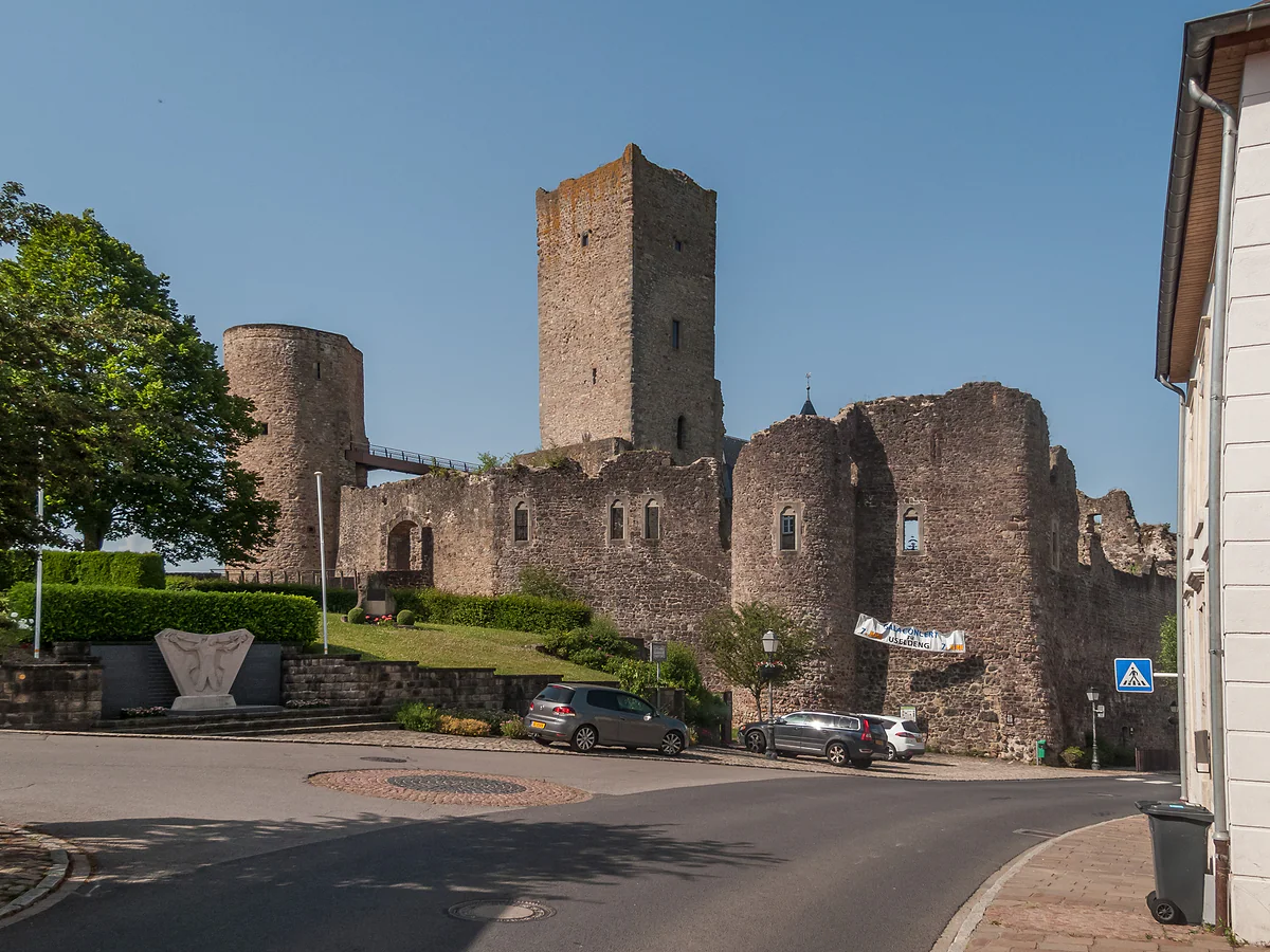 The ruins of Useldange Castle, with a square tower, round towers and walls beside the road