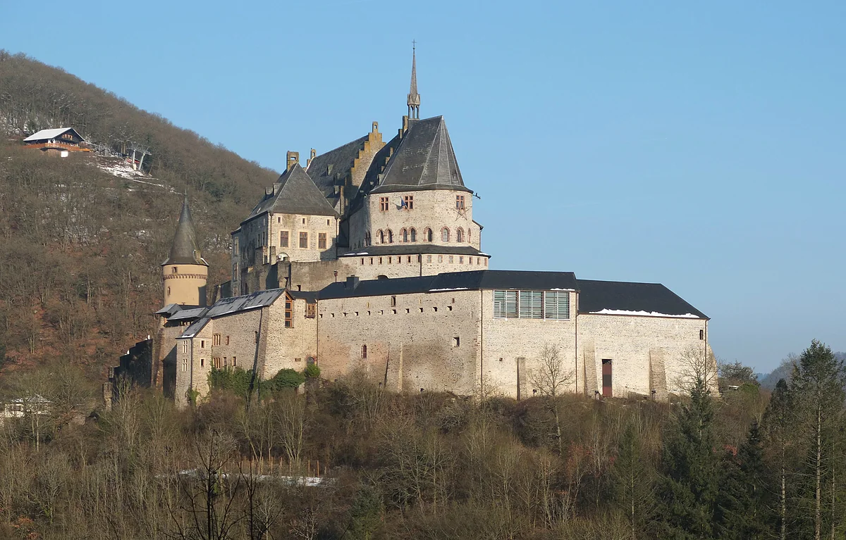 The restored Vianden Castle on its wooded hill, with slate-roofed towers and walls beneath a blue sky