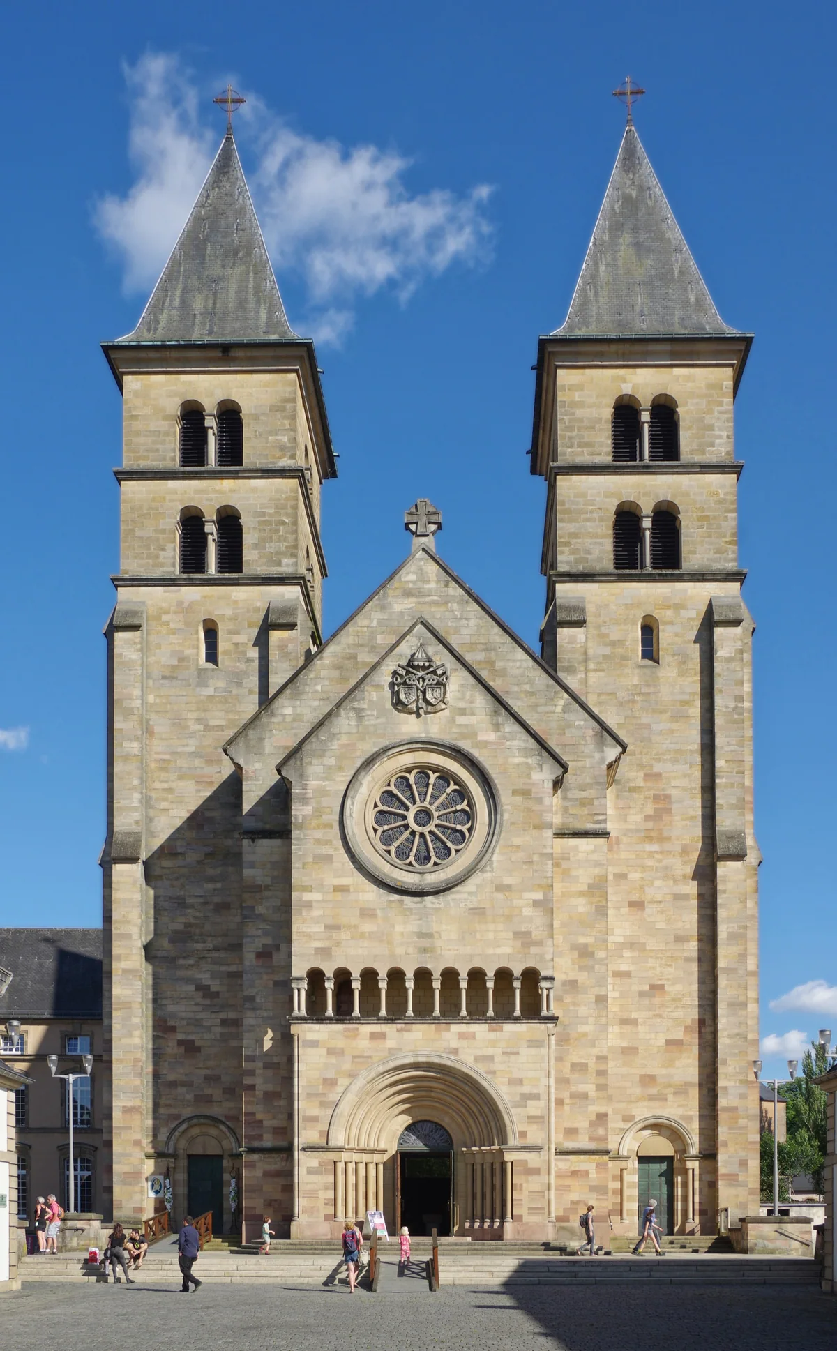 The façade of Echternach Basilica with its twin towers, rose window and doorway under a blue sky