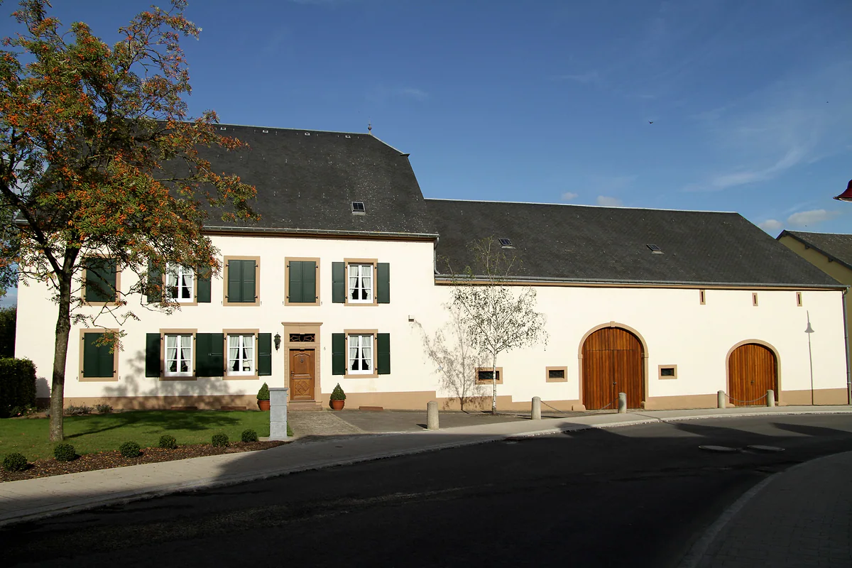 A traditional farmhouse in Grosbous, whitewashed with green shutters and two arched wooden barn doors