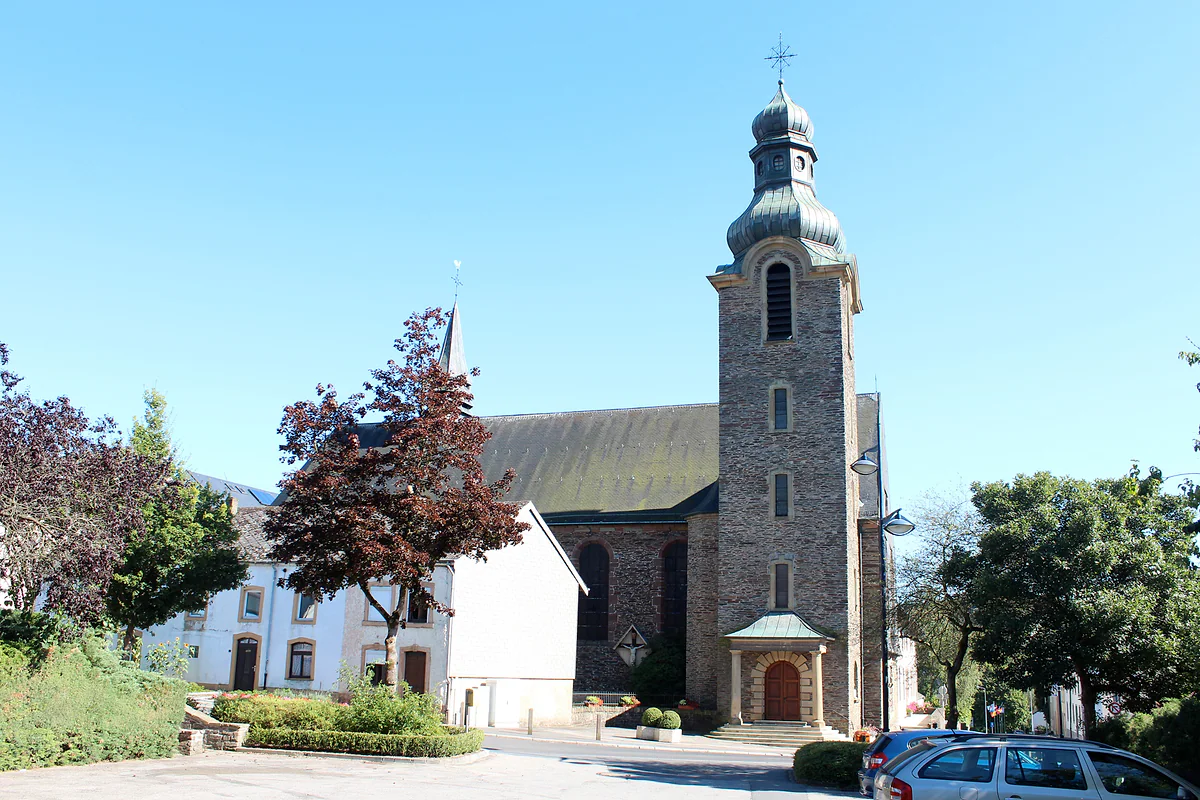 St Andrew's Church in Troisvierges, built in stone with an onion-domed bell tower, beside white houses