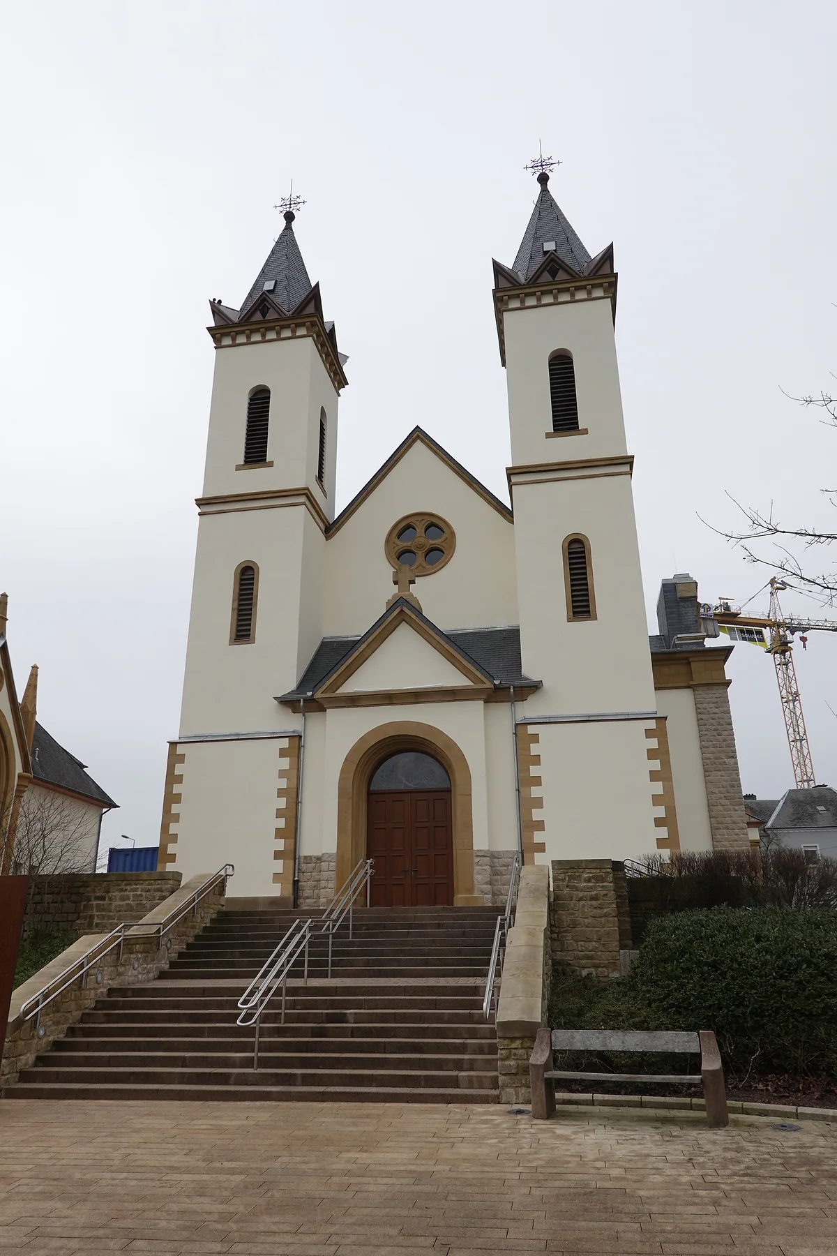 The Church of St John the Baptist in Mamer, white with twin spired towers and a flight of stone steps in front