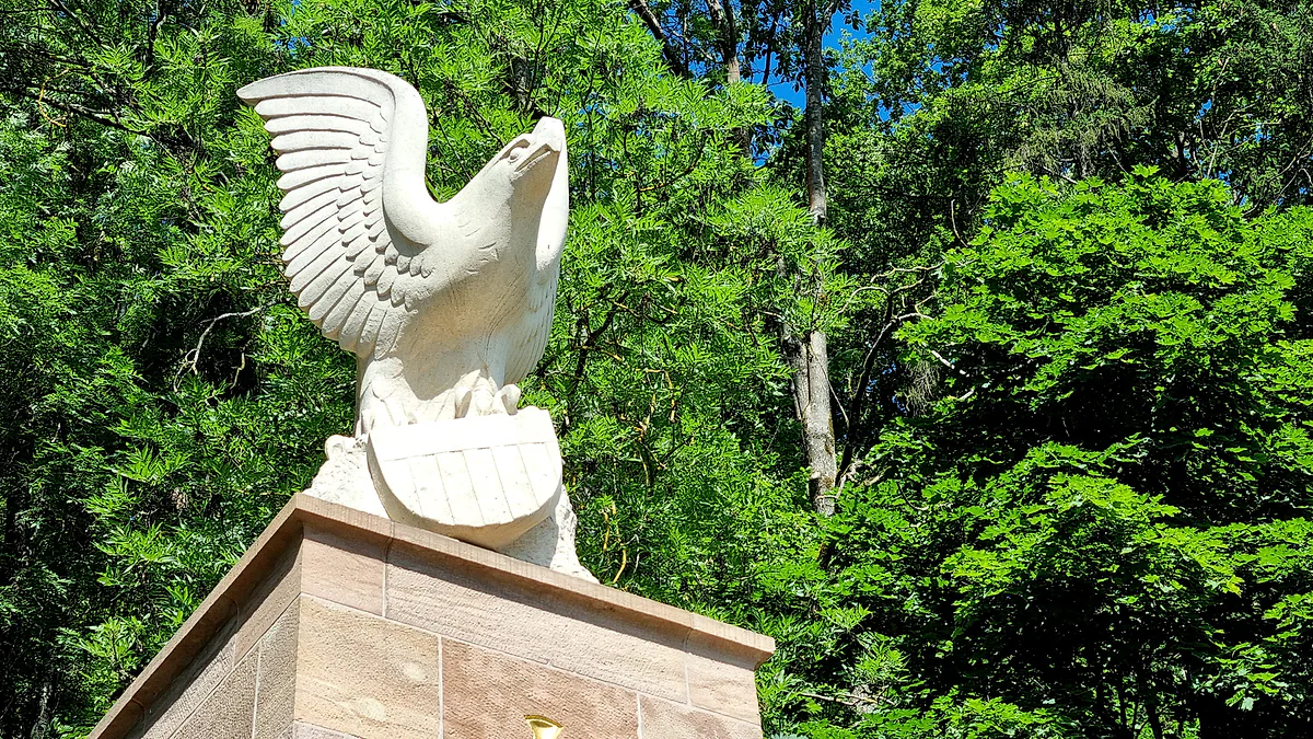 The white stone eagle of the General Patton memorial in Ettelbruck, on a plinth in front of green woodland