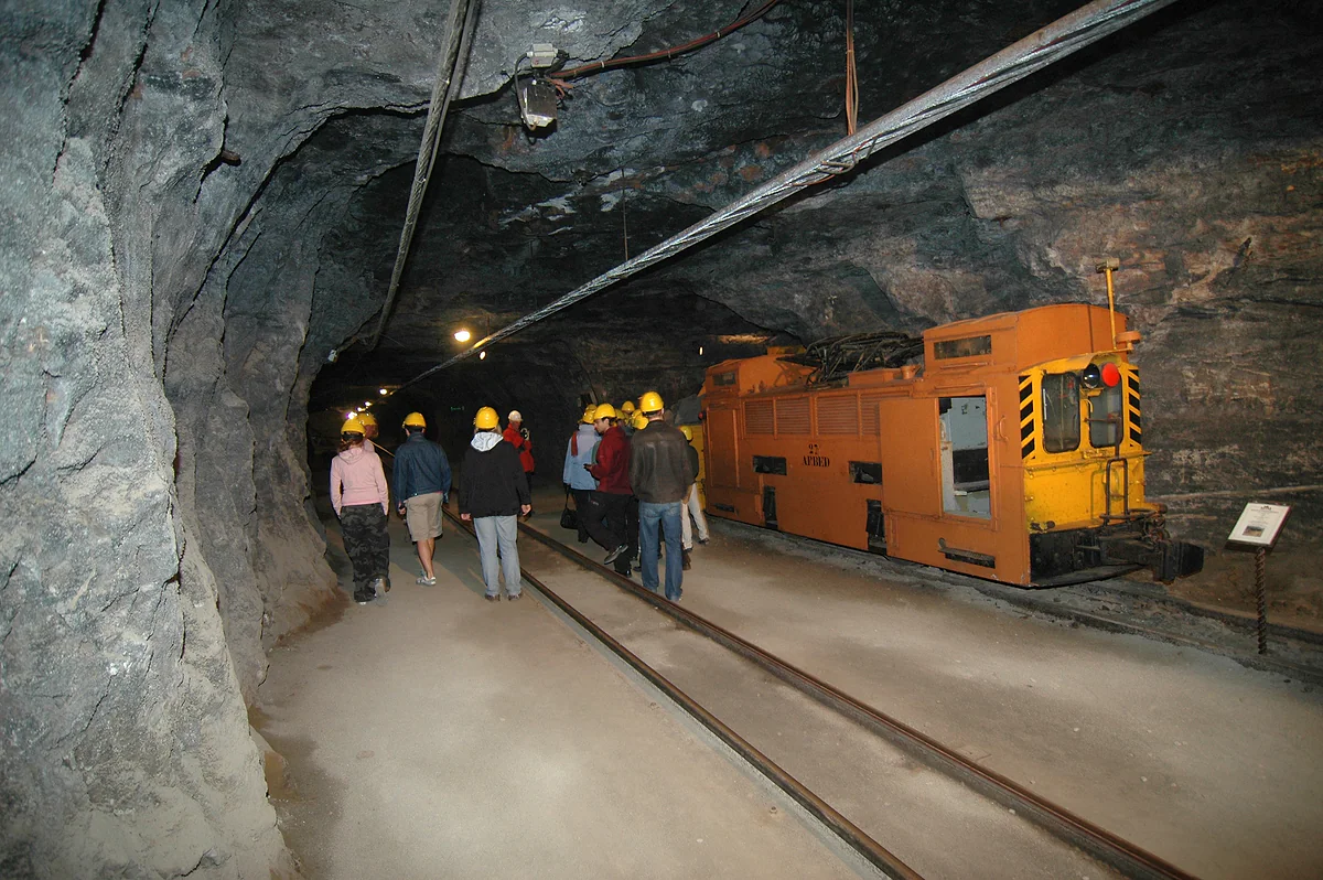 A gallery of the National Mining Museum at Rumelange, with rails, an orange mine locomotive and visitors in helmets