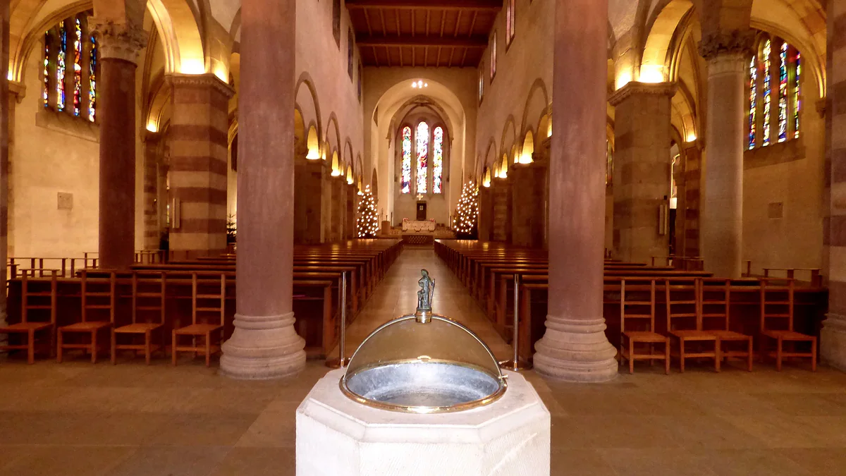 The nave of St Willibrord's Basilica in Echternach, with reddish columns, wooden pews and the font