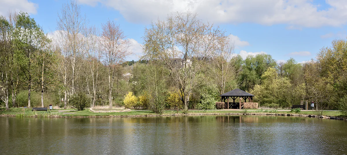 The public park at Colmar-Berg with a pond, waterside trees and a wooden pavilion by the water