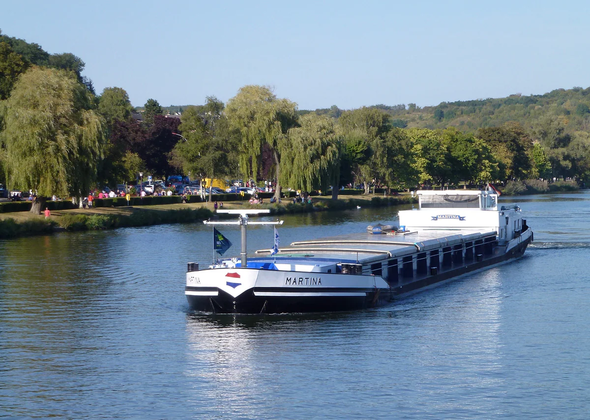 A cargo barge sailing along the Moselle at Remich, opposite the riverside promenade lined with weeping willows
