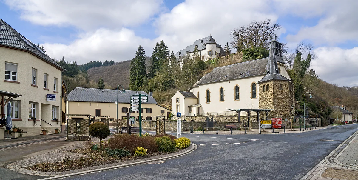 The centre of Stolzembourg with the church and its slate bell tower and the castle high on the wooded hill